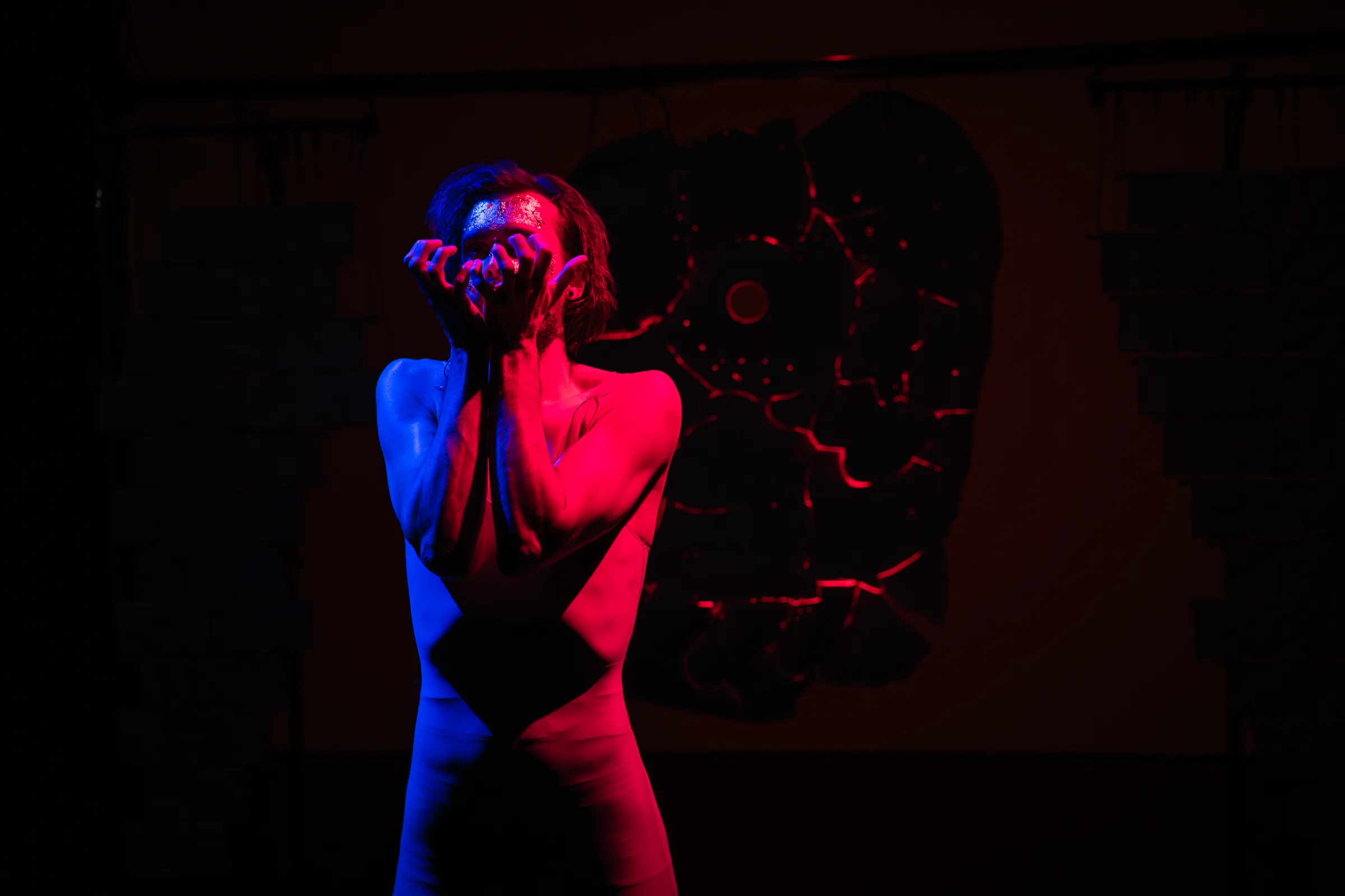 A performer lit in red and blue before a dark ceramic sculpture.