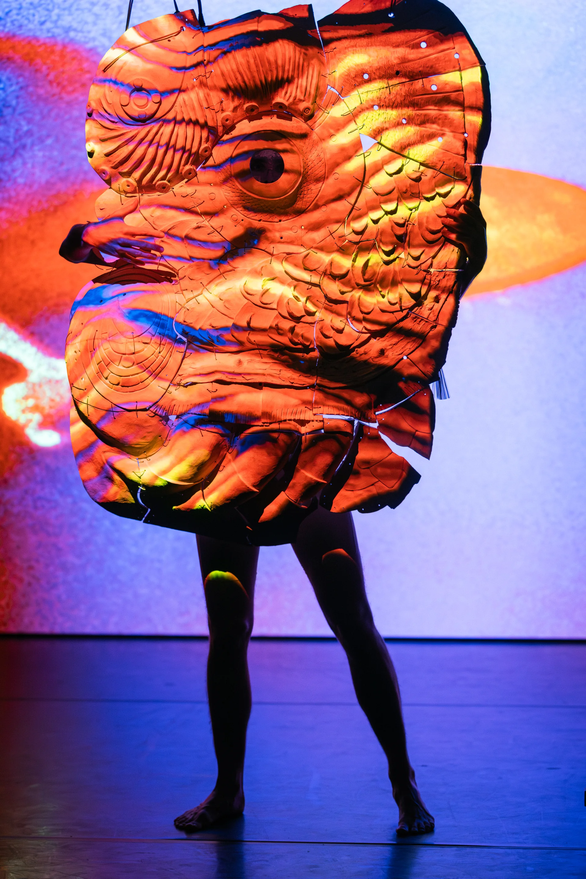 A performer stands beneath a monumental projected ceramic form.
